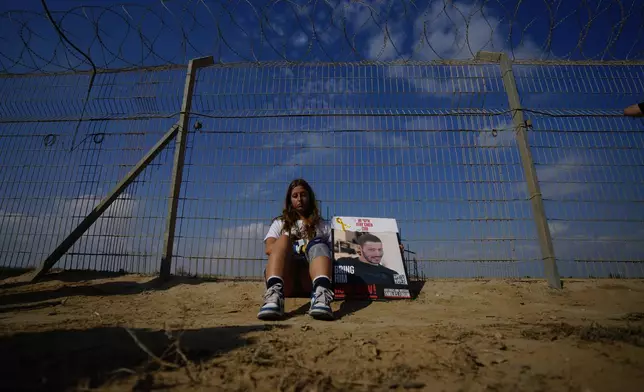 A woman sits next to a fence as relatives and friends of hostages held in the Gaza Strip by the Hamas militant group take part in a protest calling for their release in the kibbutz Nirim, southern Israel, Thursday, Aug. 29, 2024. (AP Photo/Tsafrir Abayov)