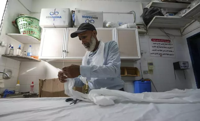 Palestinian morgue worker Nawaf al-Zuriei, a morgue worker prepares a burial shroud at at Deir al-Balah's Al-Aqsa Martyrs Hospital in the Gaza Strip, Friday, Aug. 4, 2024. Those killed by the war are considered ritually pure under Islamic tradition, so their bodies are not washed, he said. Workers cover the damaged bodies in plastic to avoid bloodstains on white shrouds. (AP Photo/Abdel Kareem Hana)