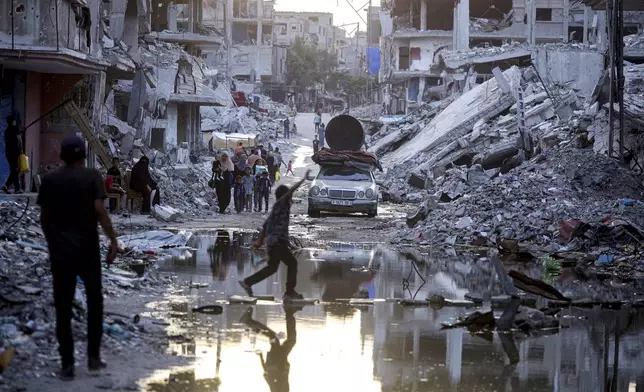 FILE - Palestinians displaced by the Israeli air and ground offensive on the Gaza Strip, walk past sewage flowing into the streets of the southern town of Khan Younis, Gaza Strip, Thursday, July 4, 2024. Health authorities and aid agencies are racing to avert an outbreak of polio in the Gaza Strip after the virus was detected in the territory's wastewater and three cases with a suspected polio symptom have been reported. (AP Photo/Jehad Alshrafi, File)