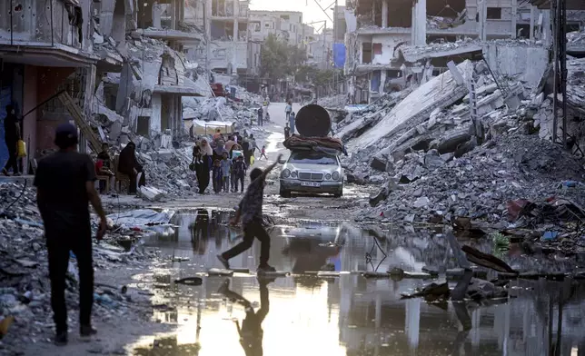 FILE - Palestinians displaced by the Israeli air and ground offensive on the Gaza Strip, walk past sewage flowing into the streets of the southern town of Khan Younis, Gaza Strip, on July 4, 2024. Israel’s military on Sunday Aug. 25, 2024 said polio vaccines for more than 1 million people had been delivered to Gaza, after the first confirmed case of the disease in the territory in a quarter-century. (AP Photo/Jehad Alshrafi, File)