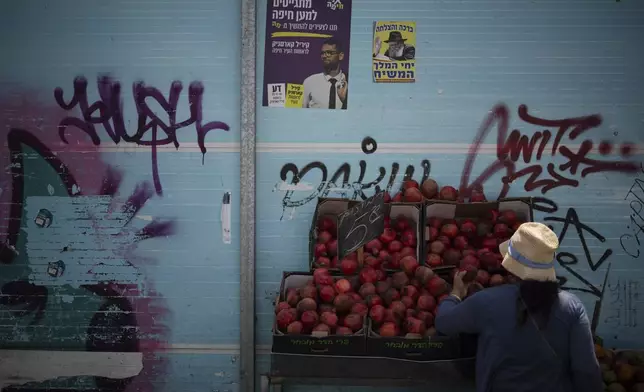 A woman checks the pomegranates displayed at a street market in Haifa, Israel, Friday, Aug. 16, 2024. Israel's economy is suffering from the nearly 11-month war with Hamas, as its leaders grind ahead with its offensive in Gaza that threatens to escalate into a wider conflict. (AP Photo/Leo Correa)