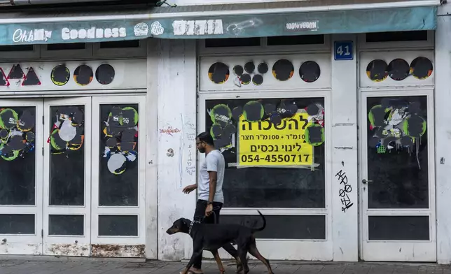 A person walks his dog past a closed shop to rent in Tel Aviv, Israel, Thursday, Aug. 15, 2024. Israel's economy is suffering from the nearly 11-month war with Hamas, as its leaders grind ahead with its offensive in Gaza that threatens to escalate into a wider conflict. (AP Photo/Ariel Schalit)