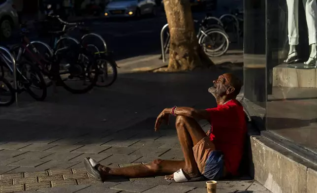 A person sits on the sidewalk next to a mall in Tel Aviv, Israel, Thursday, Aug. 15, 2024. Israel's economy is suffering from the nearly 11-month war with Hamas, as its leaders grind ahead with its offensive in Gaza that threatens to escalate into a wider conflict. (AP Photo/Ariel Schalit)