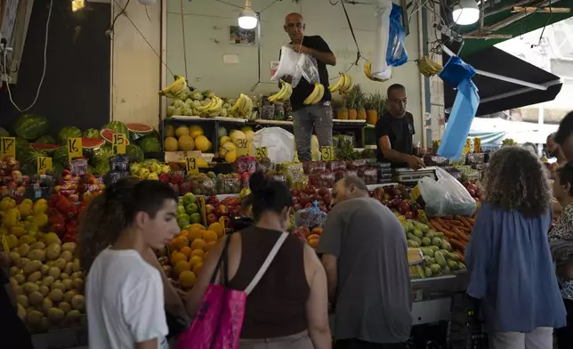 People buy fruit from a street market in Haifa, Israel, Friday, Aug. 16, 2024. Israel's economy is suffering from the nearly 11-month war with Hamas, as its leaders grind ahead with its offensive in Gaza that threatens to escalate into a wider conflict. (AP Photo/Leo Correa)