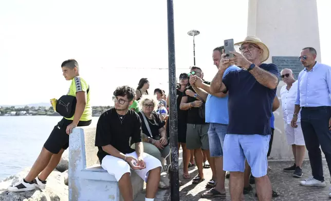 People gather at the harbor of Porticello, southern Italy, Tuesday, Aug. 20, 2024, as rescue teams and divers returned to the site of a storm-sunken superyacht to search for six people, including British tech magnate Mike Lynch, who are believed to be still trapped in the hull 50 meters (164-feet) underwater. (AP Photo/Salvatore Cavalli)