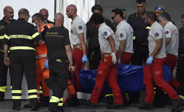 Italian Firefighters scuba divers bring ashore in a blue bag the body of one of the victims of the UK flag vessel Bayesian, Wednesday, Aug. 21, 2024. The sail yacht was hit by a violent sudden storm and sunk early Monday, while at anchor off the Sicilian village of Porticello near Palermo, in southern Italy. (AP Photo/Salvatore Cavalli)