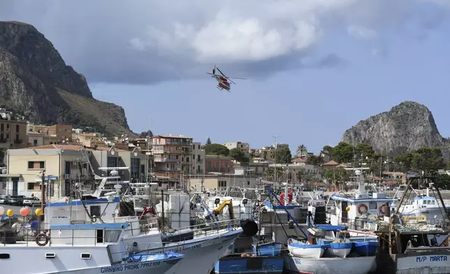 An Italian Firefighters helicopter flies over the harbor of Porticello, southern Italy, Tuesday, Aug. 20, 2024, as rescue teams and divers returned to the site of a storm-sunken superyacht to search for six people, including British tech magnate Mike Lynch, who are believed to be still trapped in the hull 50 meters (164-feet) underwater. (AP Photo/Salvatore Cavalli)