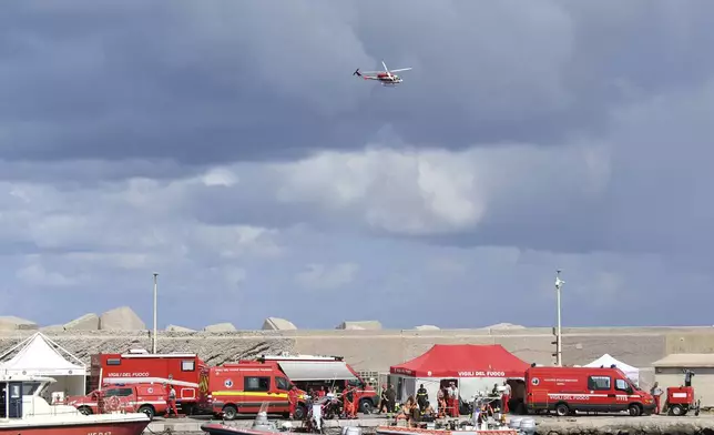 An Italian Firefighters helicopter flies over the harbor of Porticello, southern Italy, Tuesday, Aug. 20, 2024, as rescue teams and divers returned to the site of a storm-sunken superyacht to search for six people, including British tech magnate Mike Lynch, who are believed to be still trapped in the hull 50 meters (164-feet) underwater. (AP Photo/Salvatore Cavalli)