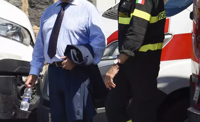 Prefect of Palermo, Massimo Mariani, left, is flanked by a firefighter as he arrives at the harbor in Porticello, Sicily, southern Italy, Thursday, Aug. 22, 2024. Divers searching the wreck of the superyacht Bayesian that sank off Sicily on Monday recovered a fifth body on Thursday and continued to search for one more as investigators sought to learn why the vessel sank so quickly. (AP Photo/Salvatore Cavalli)