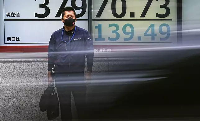 A person stands as a car passes by in front of an electronic stock board showing Japan's Nikkei index at a securities firm Tuesday, Aug. 27, 2024, in Tokyo. (AP Photo/Eugene Hoshiko)