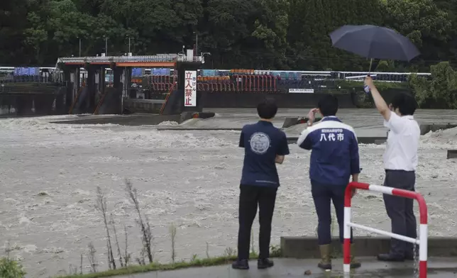 Municipal officials stand near the Kuma river, swollen due to rainfall, in Yatsushiro, southern Japan, Friday, Aug. 30, 2024, following a recent severe weather system in the area. (Hidetaka Komukai/Kyodo News via AP)