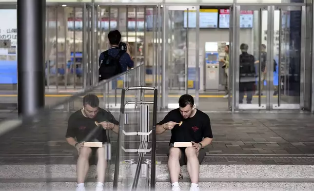 A person has a lunch box outside of the Tokaido and Sanyo Shinkansen bullet trains at Tokyo Station Friday, Aug. 30, 2024, in Tokyo, as its gate was closed due to heavy rains caused by a tropical storm. (AP Photo/Eugene Hoshiko)