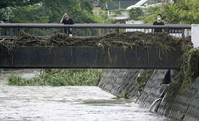 People look at debris stuck on a bridge over a river in Ninomiyamachi, southwest of Tokyo, Japan, Friday, Aug. 30, 2024, following a severe weather system in the area. (Yuya Shino/Kyodo News via AP)