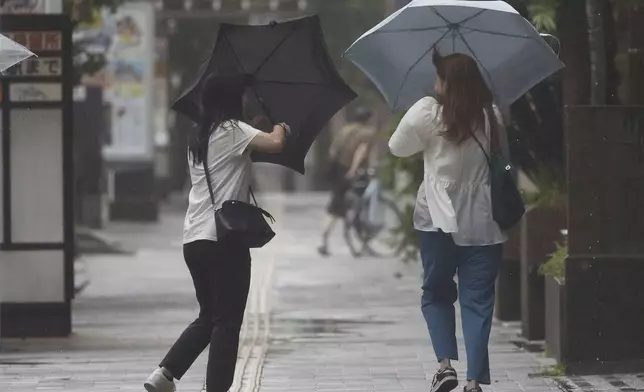 People holding umbrella, struggle with the strong wind as a typhoon is approaching in Kagoshima, western Japan, Tehursday, Aug. 29, 2024, (Hidetaka Komukai/Kyodo News via AP)