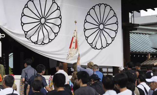 A man clad in an outdated military uniform, center, raises a Japanese flag as another prays at the main hall of the Yasukuni Shrine, in Tokyo, Japan, Thursday, Aug. 15, 2024, as the country marks the 79th anniversary of its defeat in the World War II. (AP Photo/Hiro Komae)