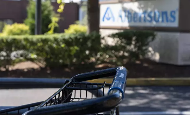 A grocery cart rests in a cart return area with a sign for Albertsons grocery store in the background on Monday, Aug. 26, 2024, in Lake Oswego, Ore. (AP Photo/Jenny Kane)