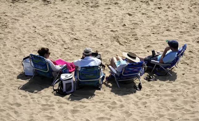 People sit on the beach, Friday, Aug. 30, 2024, in Dennis Port, Mass. (AP Photo/Michael Dwyer)