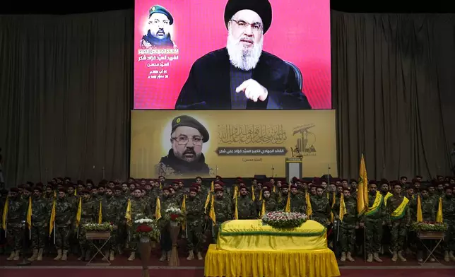 Hezbollah fighters stand behind the coffin of their top commander Fouad Shukur, who was killed by an Israeli airstrike on Tuesday, July 30, as Hezbollah leader Sayyed Hassan Nasrallah, displayed on a screen, speaks during Shukur's funeral in a southern suburb of Beirut, Lebanon, Aug. 1, 2024. (AP Photo/Hussein Malla)