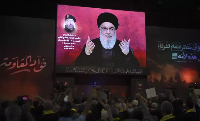 Supporters raise their fists and cheer as they watch a speech given by Hezbollah leader Sayyed Hassan Nasrallah on a screen during a ceremony to commemorate the death of top commander Fouad Shukur, who was killed by an Israeli airstrike last week, in Beirut, Lebanon, Tuesday, Aug. 6, 2024. (AP Photo/Mustafa Jamalddine)