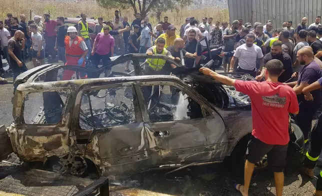 Civil Defense workers and citizens inspect the remains of a burned car that was hit by an Israeli strike in the southern port city of Sidon, Lebanon, Monday, Aug. 26, 2024. (AP Photo/Mohammed Zaatari)