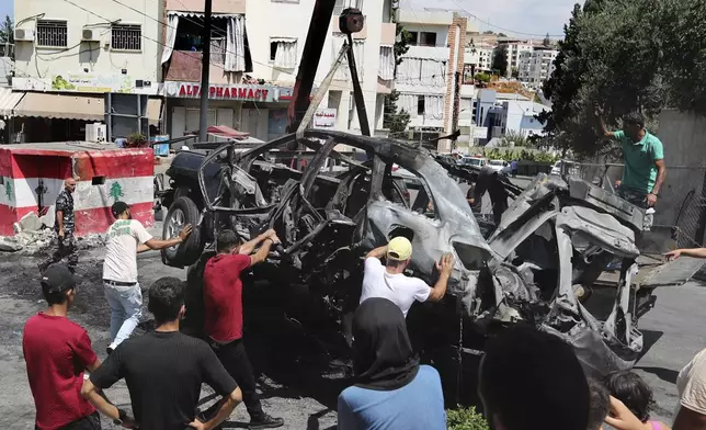 Workers use a crane to remove a car that was hit by an Israeli strike in the southern port city of Sidon, Lebanon, Wednesday, Aug. 21, 2024. (AP Photo/Mohammed Zaatari)