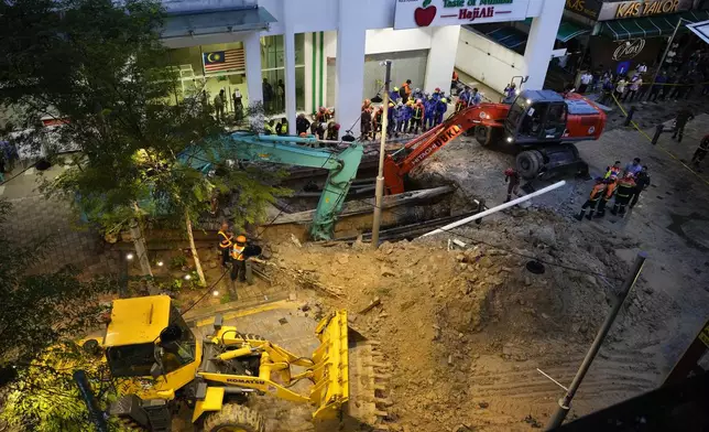 Fire and Rescue department use crane to dig after receiving reports that a woman has fallen into the sinkhole after a section of the sidewalk caved in Kuala Lumpur, Friday, Aug. 23, 2024. (AP Photo/Vincent Thian)