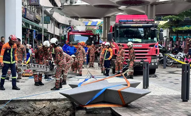 This photograph provided by Fire and Rescue Department of Malaysia, shows rescue personnel entering a deep sinkhole after receiving reports that a woman has fallen into the sinkhole after a section of the sidewalk caved in Kuala Lumpur, Friday, Aug. 23, 2024. (Fire and Rescue Department of Malaysia via AP )