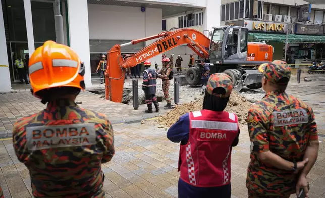 Fire and Rescue department use crane to dig a deep sinkhole after receiving reports that a woman has fallen into the sinkhole after a section of the sidewalk caved in Kuala Lumpur, Friday, Aug. 23, 2024. (AP Photo/Vincent Thian)