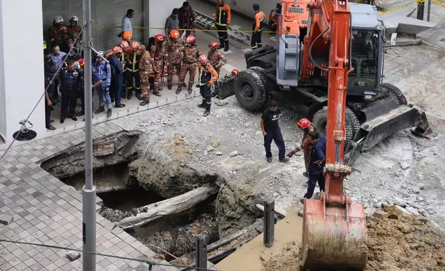 Fire and Rescue department use crane to dig after receiving reports that a woman has fallen into the sinkhole after a section of the sidewalk caved in Kuala Lumpur, Friday, Aug. 23, 2024. (AP Photo/Vincent Thian)