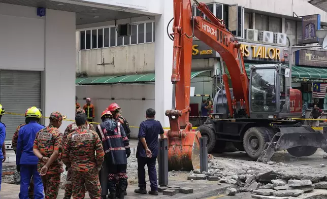 Fire and Rescue department use crane to dig a deep sinkhole after receiving reports that a woman has fallen into the sinkhole after a section of the sidewalk caved in Kuala Lumpur, Friday, Aug. 23, 2024. (AP Photo/Vincent Thian)