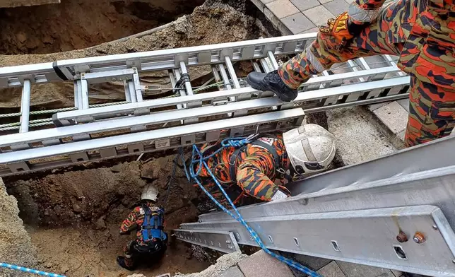 This photograph provided by Fire and Rescue Department of Malaysia, shows rescue personnel entering a deep sinkhole after receiving reports that a woman has fallen into the sinkhole after a section of the sidewalk caved in Kuala Lumpur, Friday, Aug. 23, 2024. (Fire and Rescue Department of Malaysia via AP )