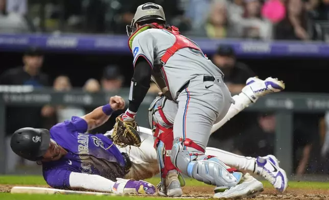 Miami Marlins catcher Nick Fortes, front, turns to put a late tag on Colorado Rockies' Nolan Jones as he scores on a throwing error in the sixth inning of a baseball game Wednesday, Aug. 28, 2024, in Denver. (AP Photo/David Zalubowski)