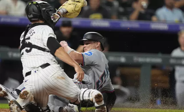 Colorado Rockies catcher Jacob Stallings, front, fields the throw as Miami Marlins' Griffin Conine scores on a sacrifice fly hit by Ali Sánchez in the sixth inning of a baseball game Tuesday, Aug. 27, 2024, in Denver. (AP Photo/David Zalubowski)