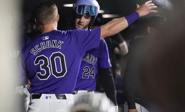 Colorado Rockies' Aaron Schunk (30) hugs Ryan McMahon (24) who returns to the dugout after hitting a solo home run off Miami Marlins starting pitcher Edward Cabrera in the sixth inning of a baseball game Monday, Aug. 26, 2024, in Denver. (AP Photo/David Zalubowski)