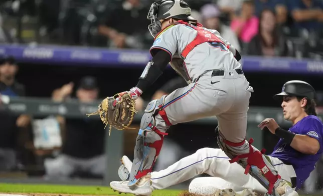 Miami Marlins catcher Nick Fortes, front, pursues an errant throw from shortstop Otto Lopez as Colorado Rockies' Michael Toglia, far right, scores in the sixth inning of a baseball game Wednesday, Aug. 28, 2024, in Denver. (AP Photo/David Zalubowski)