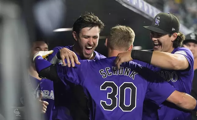 Colorado Rockies' Aaron Schunk, center, is congratulated by teammates Nolan Jones, left, and Michael Toglia after hitting his first home run of the major leagues, a solo shot off Miami Marlins starting pitcher Max Meyer, in the fifth inning of a baseball game Wednesday, Aug. 28, 2024, in Denver. (AP Photo/David Zalubowski)