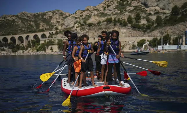 Children attend a swimming camp organized by the Grand Bleu Association which facilitates access to the sea for marginalized children in Marseille, France, Friday, July 26, 2024. Marseille, a millennia-old port, is a crossroads of cultures and faiths, where the sea is ever present but not equally accessible, and the beauty and cosmopolitan flair rub shoulders with enclaves of poverty and exclusion even more intimately than in the rest of France. (AP Photo/Daniel Cole)