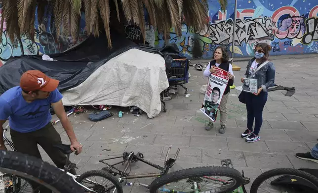 Catholic nun Paola Clericó, holding a poster of missing person Fernando Ivan Ornelas, and Veronica Rosas with a photo of her missing son Diego, ask a resident if he recognizes either man and invite him to join a Mass with members of their search collective "Uniendo Esperanzas" or Uniting Hope, in Mexico City, Sunday, July 21, 2024. The collective of people with missing family members held a Mass on the birthday of Ornelas who disappeared five years prior. (AP Photo/Ginnette Riquelme)