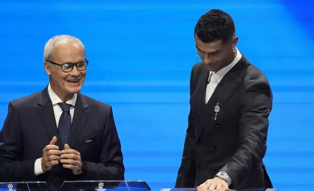 UEFA's Giorgio Marchetti watches player Cristiano Ronaldo press a button to proceed with the Champions League, league phase, draw, in Monaco, Thursday, Aug. 29, 2024. (AP Photo/Gregorio Borgia)