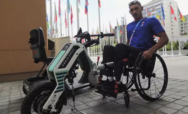 Qatari para-athlete Ali Radi Arshid poses near a motorized device that pulls wheelchair users in the Paralympic Village, Saturday, Aug. 24, 2024, in Saint-Ouen, France. (AP Photo/Tom Nouvian)