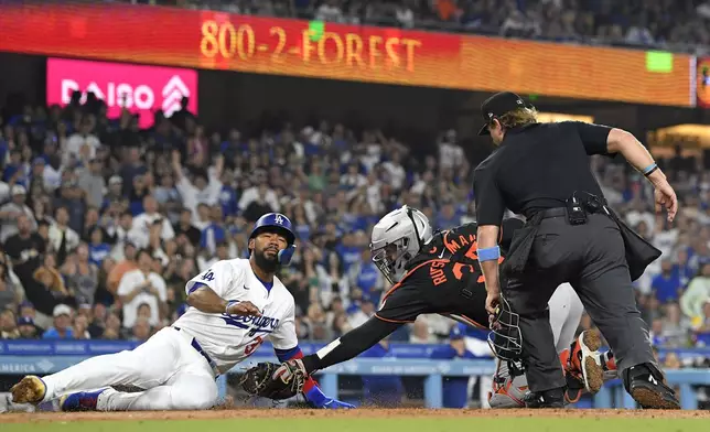 Los Angeles Dodgers' Teoscar Hernández, left, is tagged out by Baltimore Orioles catcher Adley Rutschman, center, as he tries to score on a single by Miguel Rojas while home plate umpire Mike Muchlinski watches during the fourth inning of a baseball game Thursday, Aug. 29, 2024, in Los Angeles. (AP Photo/Mark J. Terrill)