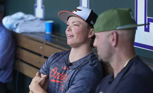 Retired Major League Baseball player Matt Holliday, front, listens as his son, Jackson, second baseman for the Baltimore Orioles, talks to reporters before the Orioles face the Colorado Rockies in a baseball game Friday, Aug. 30, 2024, in Denver. (AP Photo/David Zalubowski)