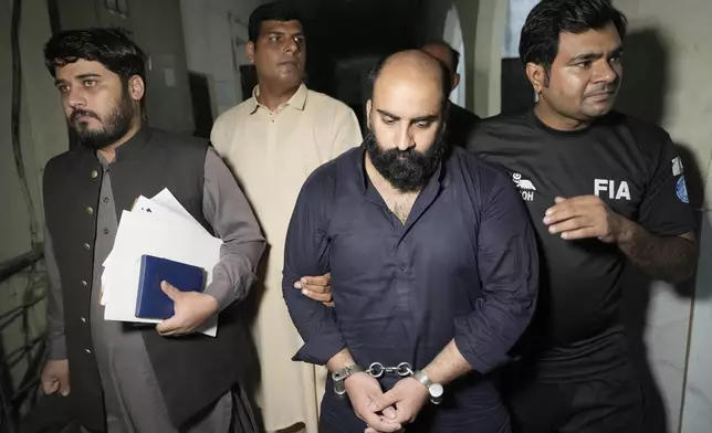 Farhan Asif, center, a freelance web developer who was arrested and charged with cyber terrorism for his alleged role in spreading misinformation that led to widespread rioting in the U.K. earlier this month, is escorted by officials for his court appearance, in Lahore, Pakistan, Monday, Aug. 26, 2024. (AP Photo/K.M. Chaudary)