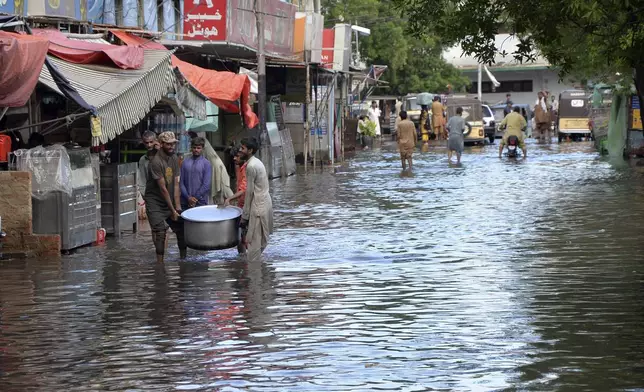 People wade through a flooded road caused by heavy monsoon rain, in Hyderabad, Pakistan, Friday, Aug. 30, 2024. (AP Photo/Pervez Masih)