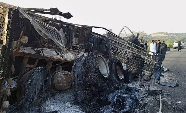 People look at a burnt vehicle which was torched by gunmen after they killed passengers at a highway in Musakhail, a district in Baluchistan province in restive southwestern Pakistan, Monday, Aug. 26, 2024. (AP Photo/Rahmat Khan)