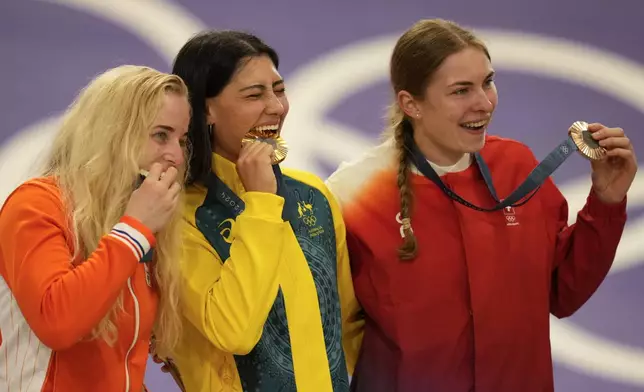 Saya Sakakibara of Australia, centre, bites her gold medal of the women's BMX, flanked by silver medallist Manon Veenstra of Netherlands, left, and bronze medallist Zoe Claessens of Switzerland, at the 2024 Summer Olympics, Friday, Aug. 2, 2024, in Saint-Quentin-en-Yvelines, France (AP Photo/Ricardo Mazalan)