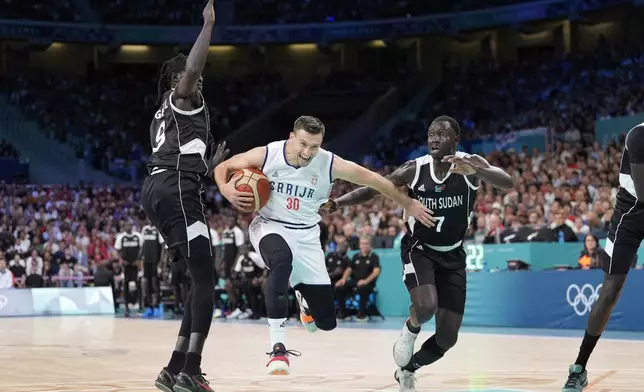 Serbia's Aleksa Avramovic, center, jumps between South Sudan's Wenyen Gabriel, left, and South Sudan's Bul Kuol during a men's basketball game at the 2024 Summer Olympics, Saturday, Aug. 3, 2024, in Villeneuve-d'Ascq, France. (AP Photo/Michael Conroy)