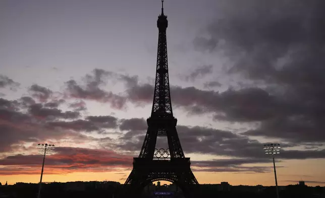 The sun sets behind the Eiffel Tower during play in the women's beach volleyball bronze medal match between Australia and Switzerland, at the 2024 Summer Olympics, Friday, Aug. 9, 2024, in Paris, France. (AP Photo/Louise Delmotte)