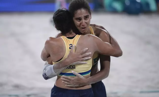 Brazil's Ana Patricia Silva Ramos, facing, hugs teammate Eduarda "Duda" Santos Lisboa as they celebrate winning the women's beach volleyball gold medal match against Canada, at the 2024 Summer Olympics, Friday, Aug. 9, 2024, in Paris, France. (AP Photo/Louise Delmotte)