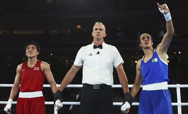 Janjaem Suwannapheng of Thailand, left, looks on after Match Referee Shawn Reese raises the arm of Imane Khelif of Algeria to announce the winner of their women's 66kg semifinal boxing match, at the 2024 Summer Olympics, Tuesday, Aug. 6, 2024, in Paris, France. (Richard Pelham/Pool Photo via AP)